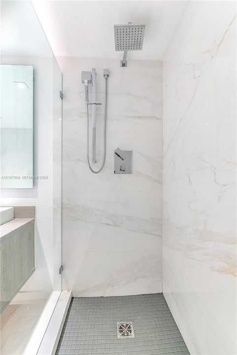 Walk-in shower featuring large-format stone wall tiling, a rainfall showerhead, a separate handheld sprayer, a glass enclosure, and a mosaic-tiled floor