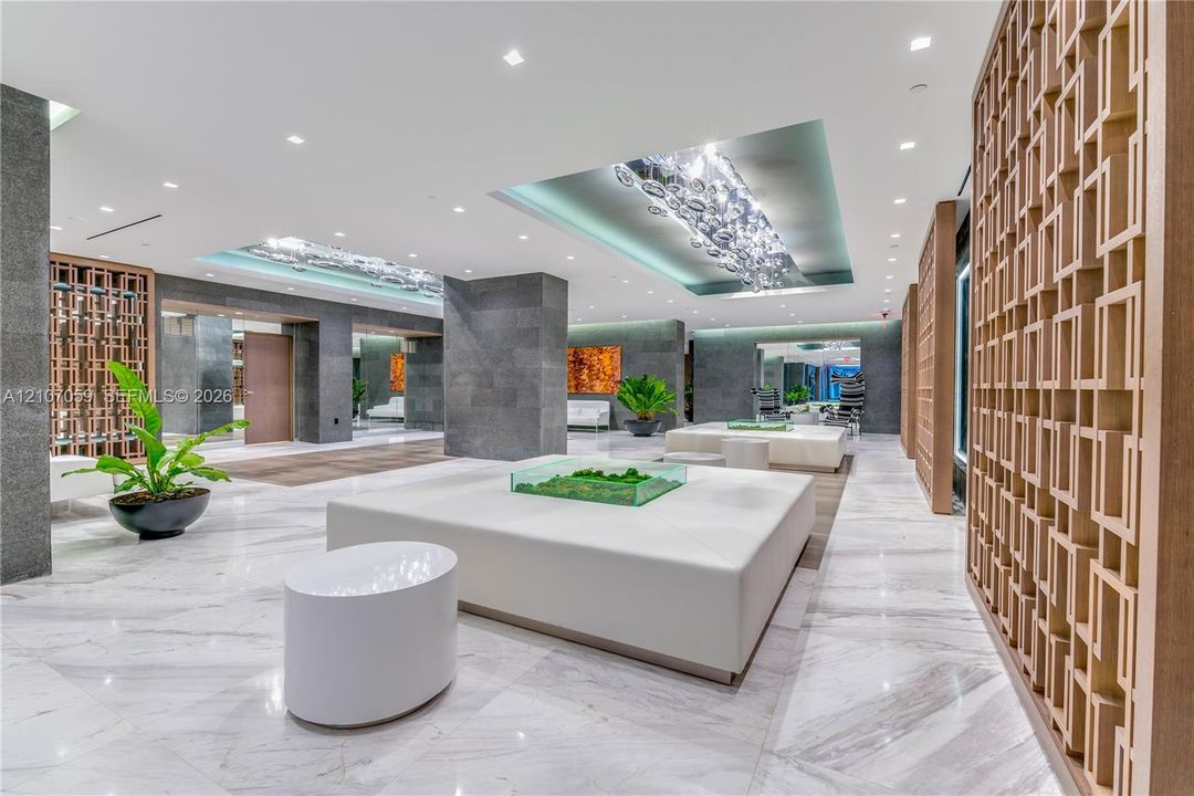 Polished stone flooring, geometric wood-finish privacy screens, recessed tray ceilings with custom glass light fixtures, and stone-clad architectural columns