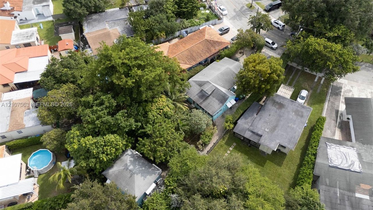 Aerial perspective of a residential lot featuring mature trees, landscaped grounds, concrete driveway, and shingle roofing