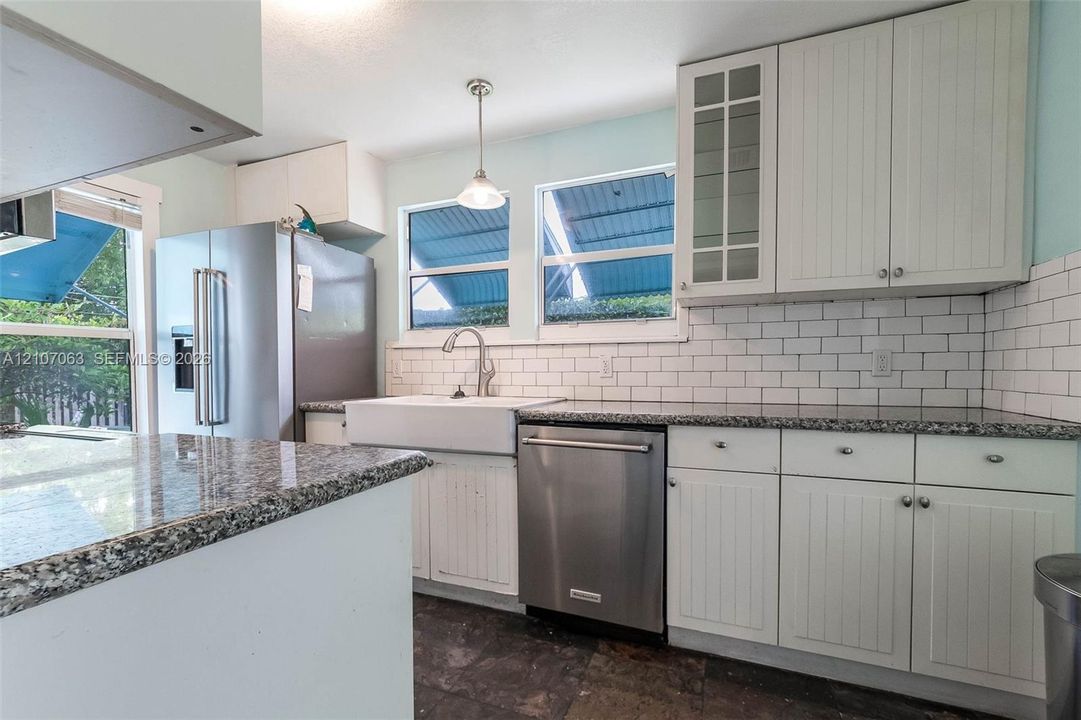 Kitchen featuring white cabinetry with glass-panel upper doors, stone-finish countertops, white subway tile backsplash, farmhouse-style sink, and stainless steel appliances