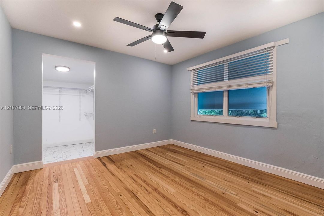 Room featuring wood-finish flooring, a ceiling fan with integrated lighting, horizontal blinds, and a walk-in closet