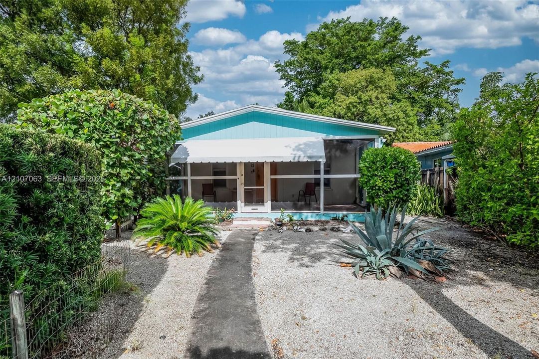 Exterior featuring a turquoise facade, covered screened porch, metal awning, and landscaped yard with decorative gravel and mature shrubbery