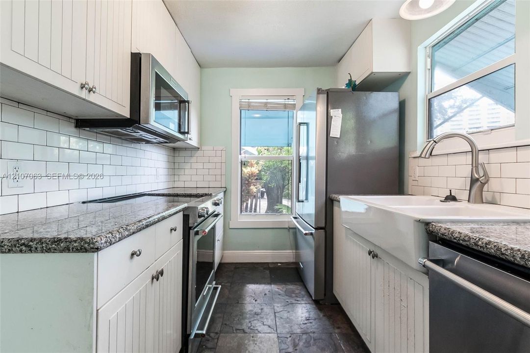 Kitchen featuring white beadboard cabinetry, stone countertops, white subway tile backsplash, farmhouse-style sink, and slate-finish flooring