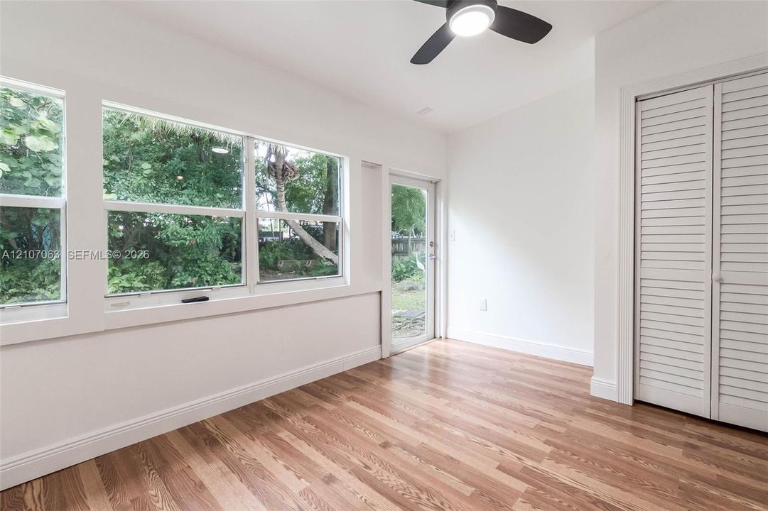 Wood-finish flooring, large windows, louvered closet doors, and ceiling fan with integrated lighting