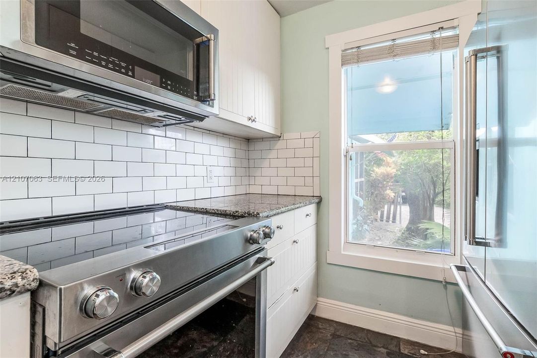 Kitchen featuring stainless steel appliances, stone-finish countertops, white shaker-style cabinetry, and a subway tile backsplash