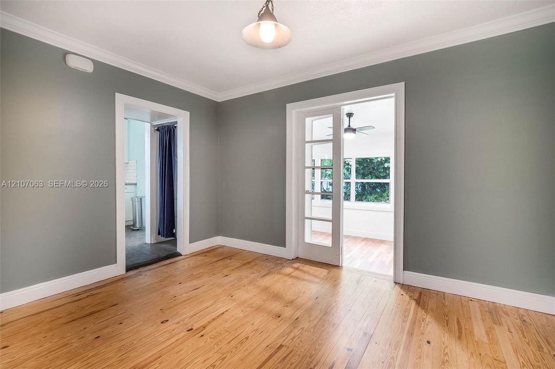 Room featuring wood-finish flooring, crown molding, a hanging pendant light, and a glass-paneled French door