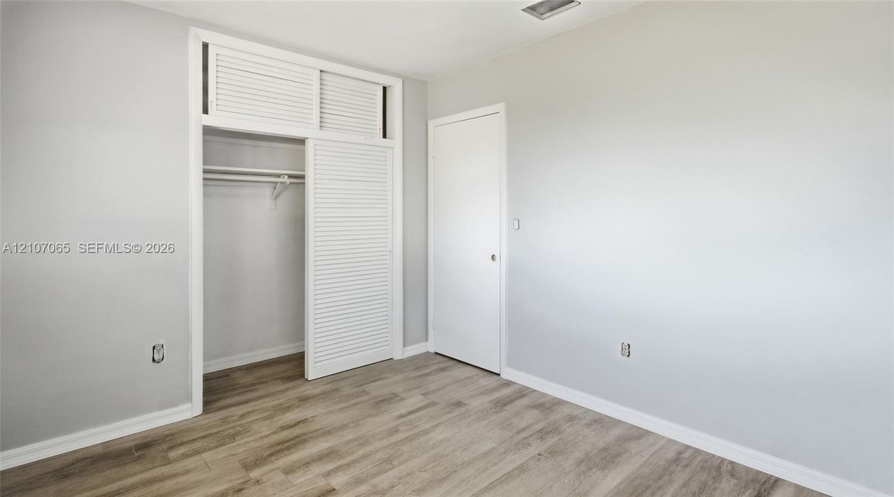 Interior room featuring wood-finish flooring, neutral wall paint, and a sliding louvered closet door with overhead storage
