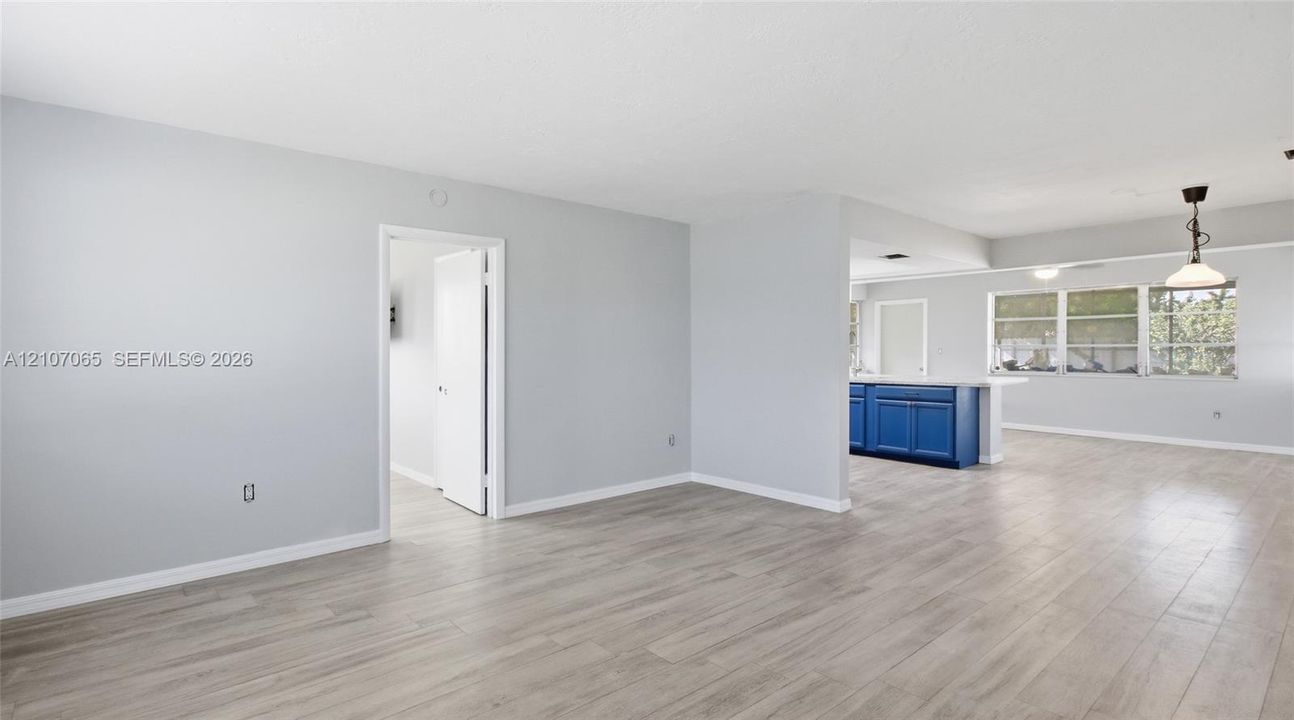 Open floor plan featuring wood-finish flooring, neutral wall paint, multi-pane windows, and a peninsula-style kitchen counter with blue cabinetry