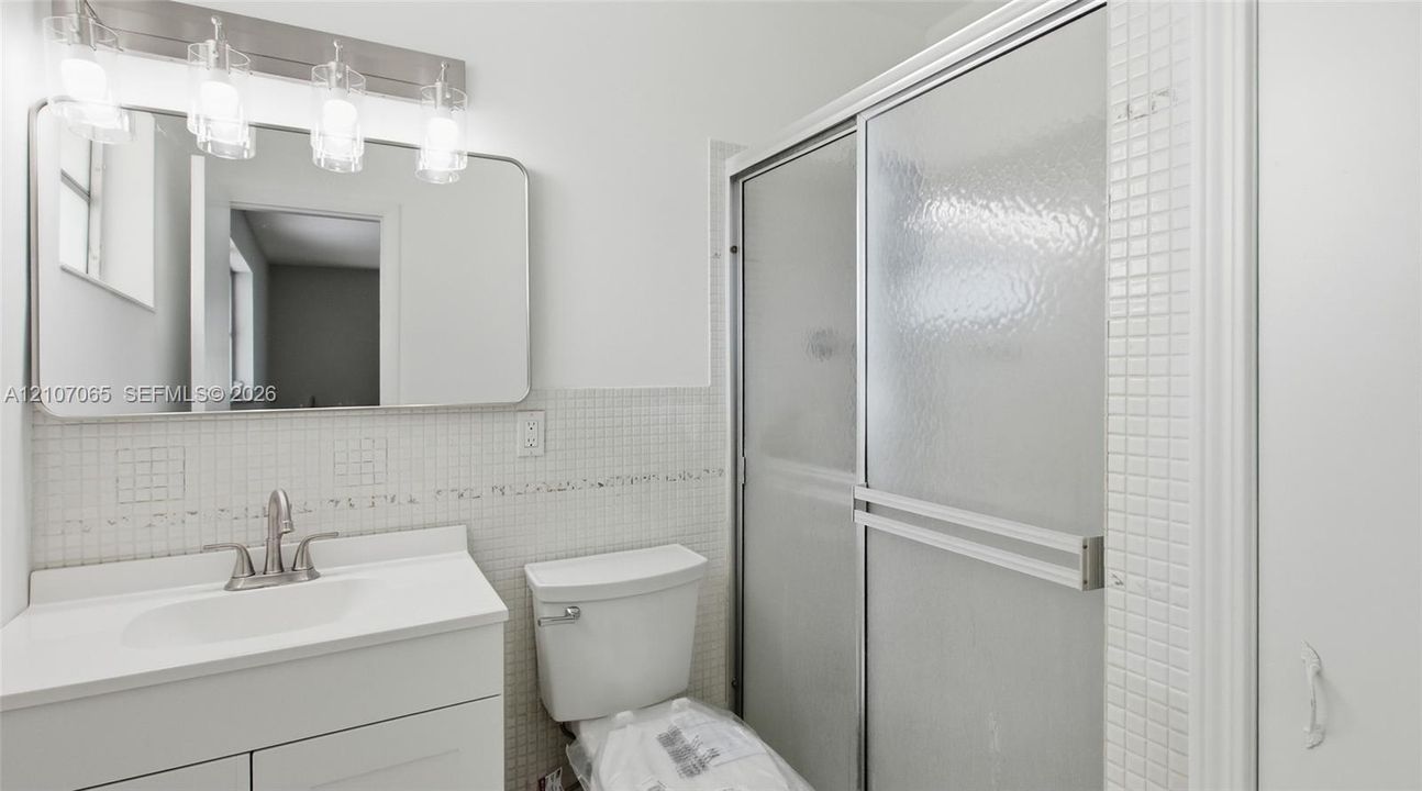 Bathroom featuring a white vanity cabinet, square wall-mounted mirror, four-light vanity fixture, and a shower enclosure with sliding glass doors