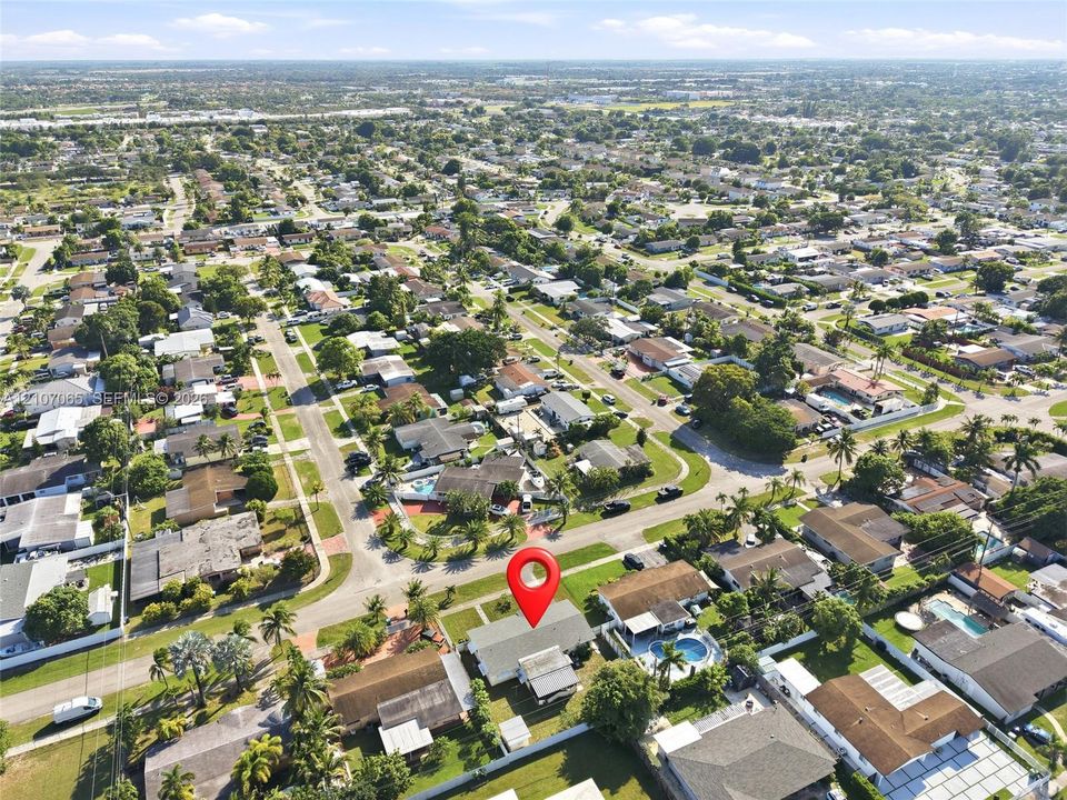 Aerial perspective of a corner lot residence featuring a shingled roof, paved driveway, and established perimeter landscaping
