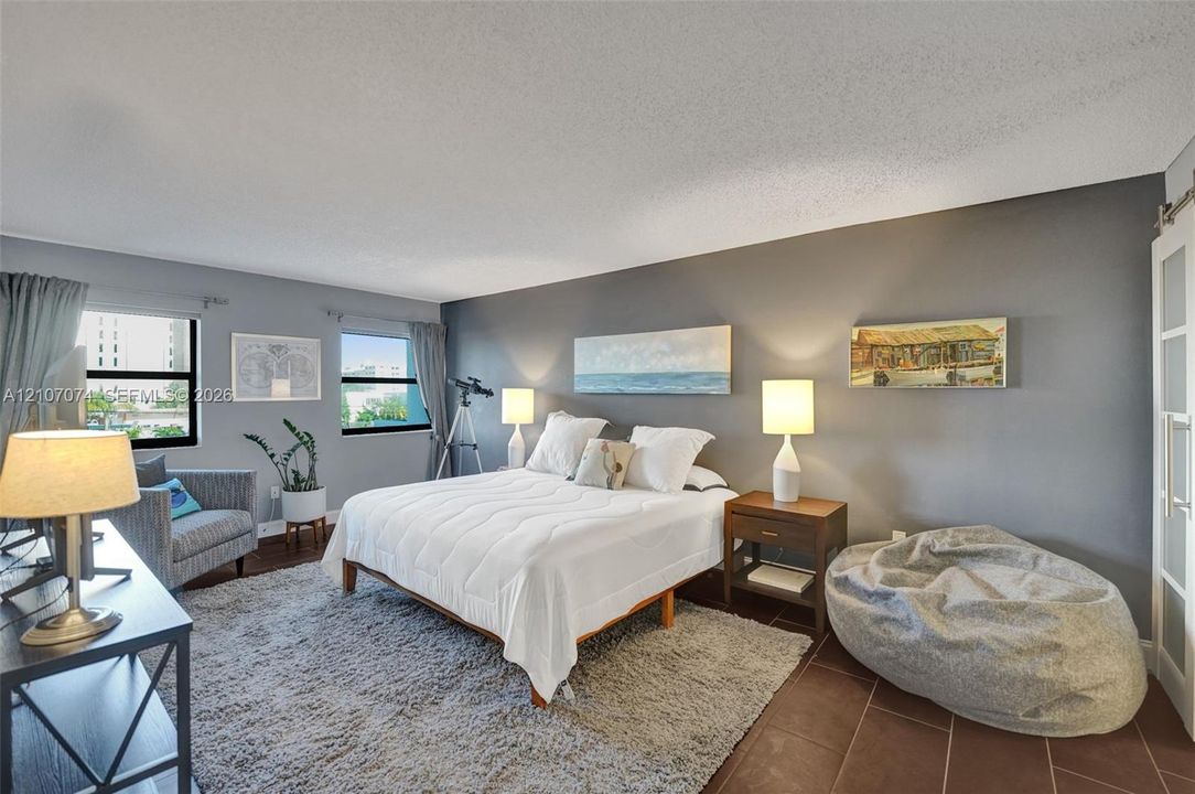 Bedroom featuring large dual windows, matte grey wall finish, and a sliding frosted glass paneled door