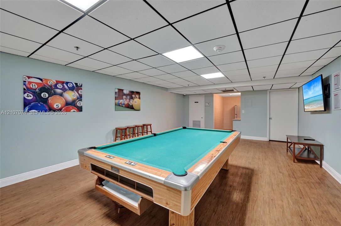 Finished recreation room featuring wood-finish flooring, a drop ceiling with recessed panel lighting, and solid-core interior doors