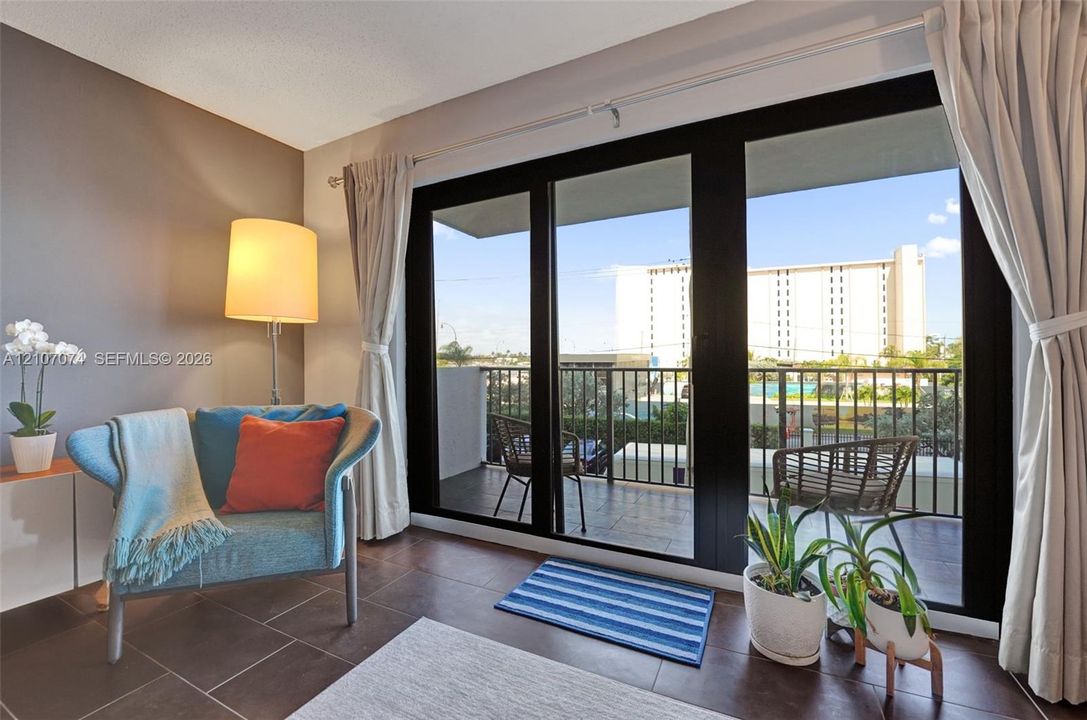 Large black-framed sliding glass doors opening to a private balcony with metal railings and tile flooring