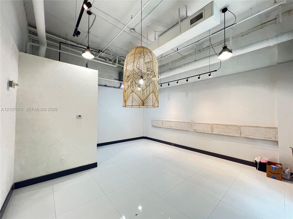Industrial-style interior featuring white tiled flooring, an exposed structural ceiling with track lighting, a large woven pendant fixture, and built-in wall-mounted shelving
