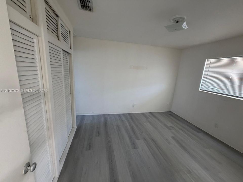 Room featuring wood-finish flooring, floor-to-ceiling louvered-style closets with overhead storage, and a window with horizontal blinds