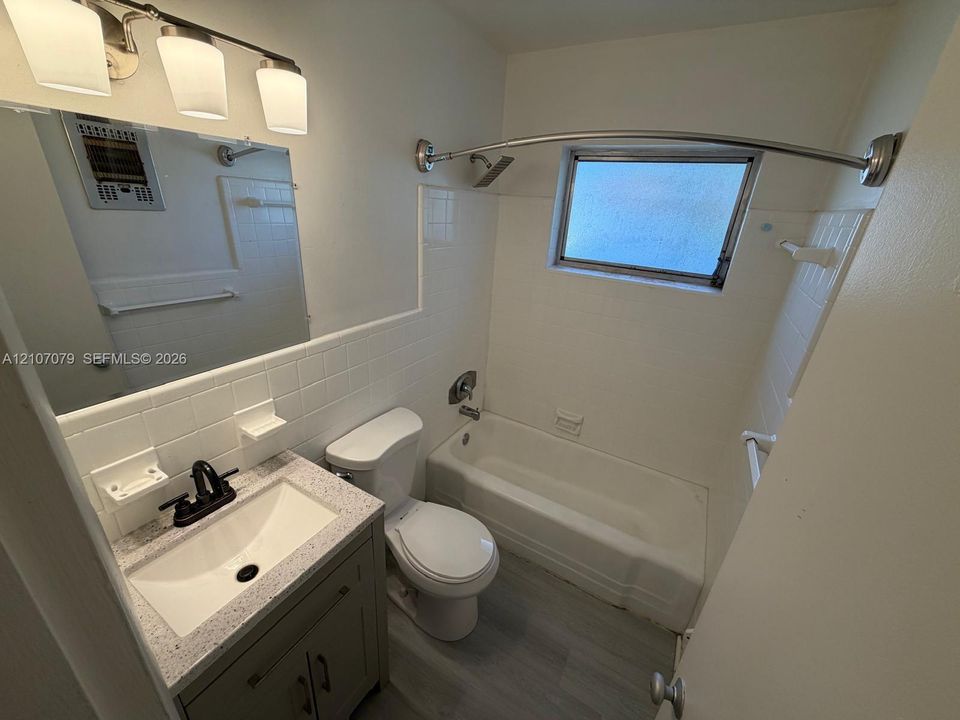 Bathroom featuring a vanity with a rectangular sink and stone-finish countertop, matte black faucet, wall-mounted light fixture, and a shower-tub combination with white tile surround