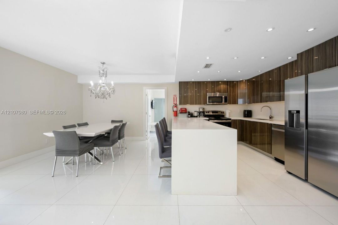 Kitchen featuring high-gloss cabinetry, stone-surface breakfast bar, polished tile flooring, stainless steel appliances, and crystal chandelier lighting