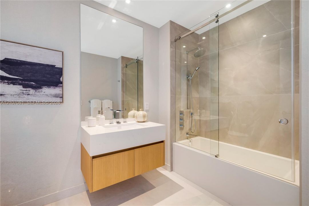 Floating wood-finish vanity with a rectangular sink, large format tile shower surround, glass sliding shower door, and wall-mounted oversized mirror