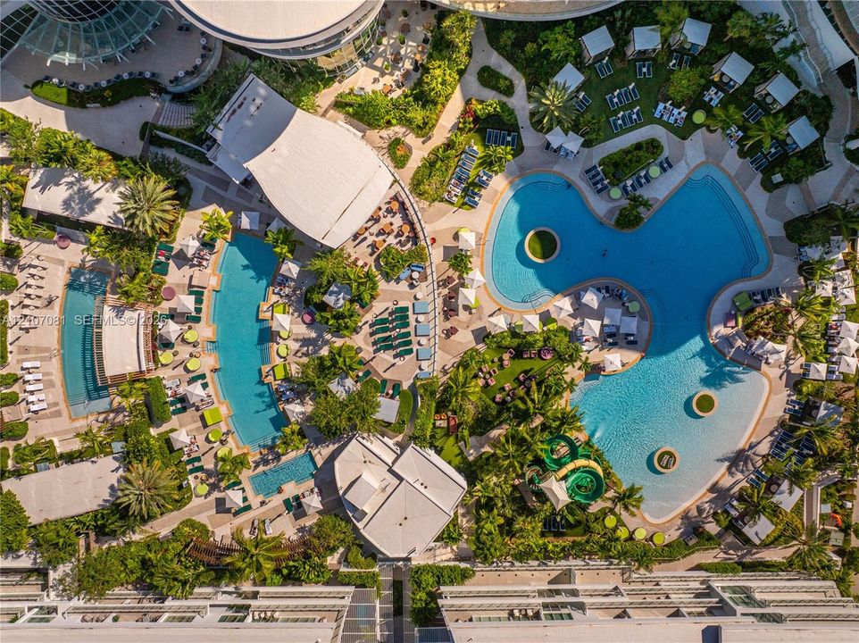 Expansive aquatic complex featuring multiple swimming pools, integrated water slide, paved patio surrounds, and mature landscaping