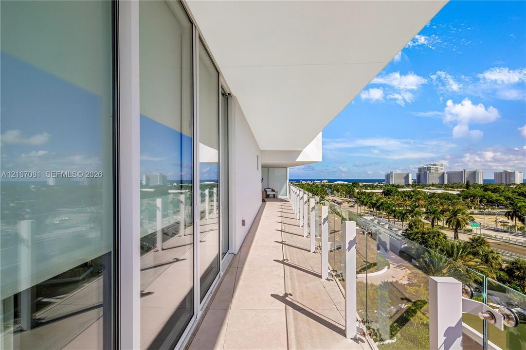 Covered balcony featuring expansive floor-to-ceiling glass doors, tile flooring, and a frameless glass railing