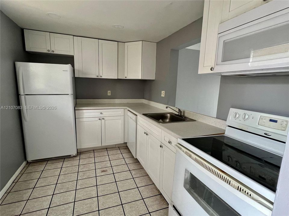 Kitchen featuring white shaker-style cabinetry, solid-surface countertops, a stainless steel undermount sink, and tiled flooring