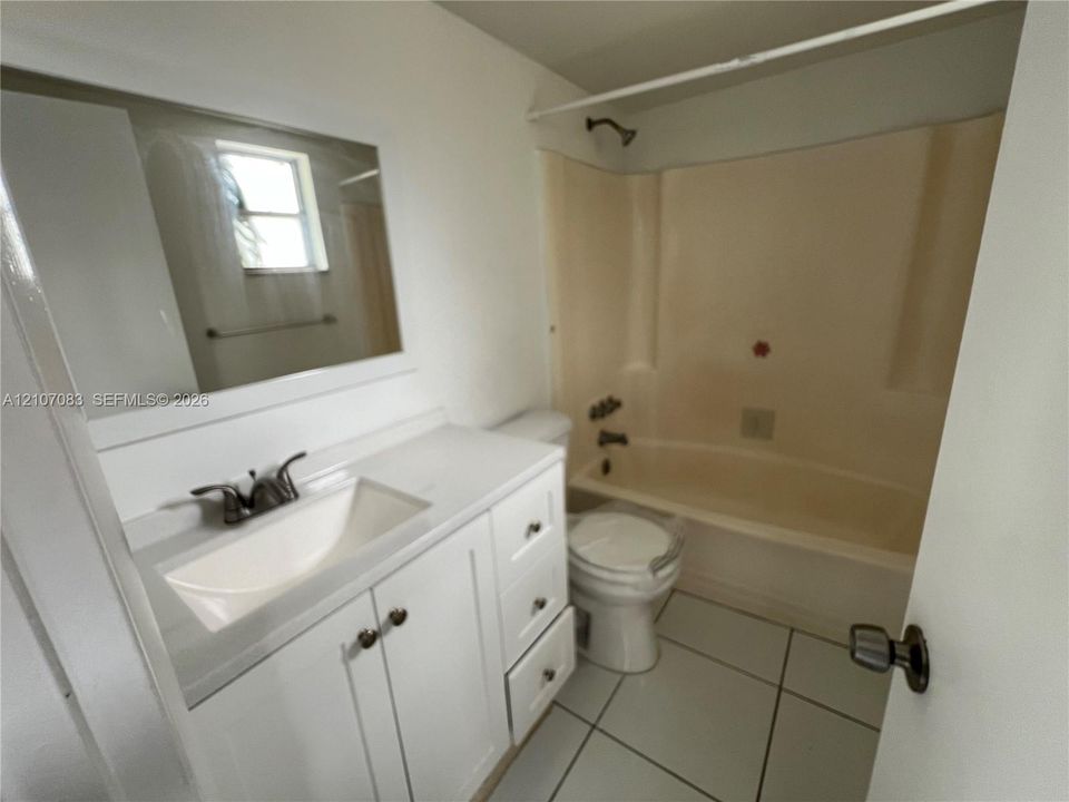 Bathroom featuring a white vanity with integrated sink, rectangular wall mirror, tile flooring, and a combined tub and shower enclosure