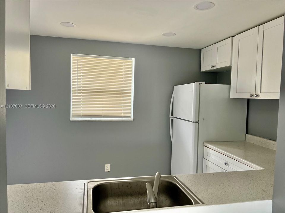 Kitchen featuring white shaker-style cabinetry, solid-surface countertops, a stainless steel undermount sink, recessed lighting, and a window