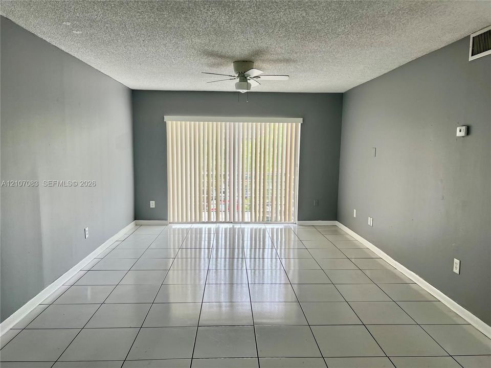 Neutral-toned walls, tile flooring, and ceiling fan with integrated lighting, featuring floor-to-ceiling vertical blinds covering the sliding glass door