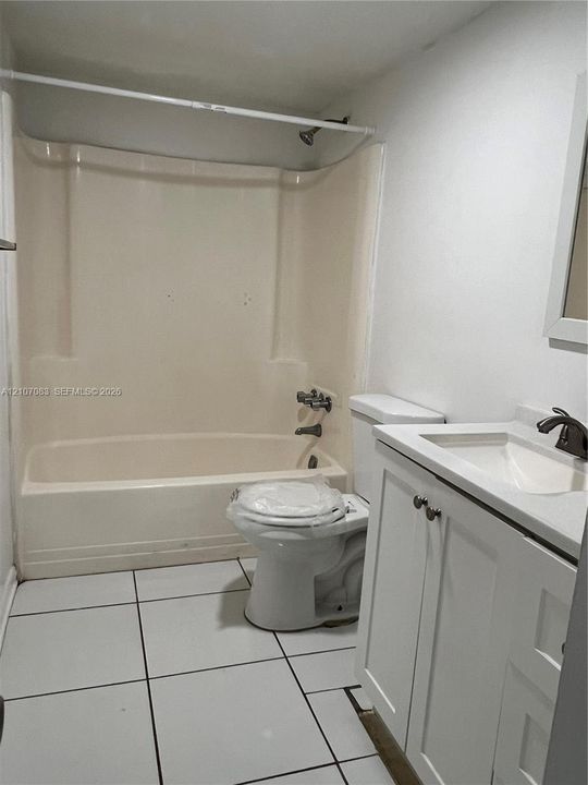Bathroom featuring a white vanity cabinet with an integrated sink, polished metal faucet, tiled flooring, and a composite tub and shower surround