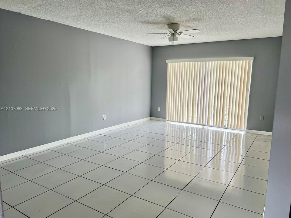 Neutral interior space featuring polished tile flooring, light grey walls, a ceiling fan with light fixture, and vertical window blinds