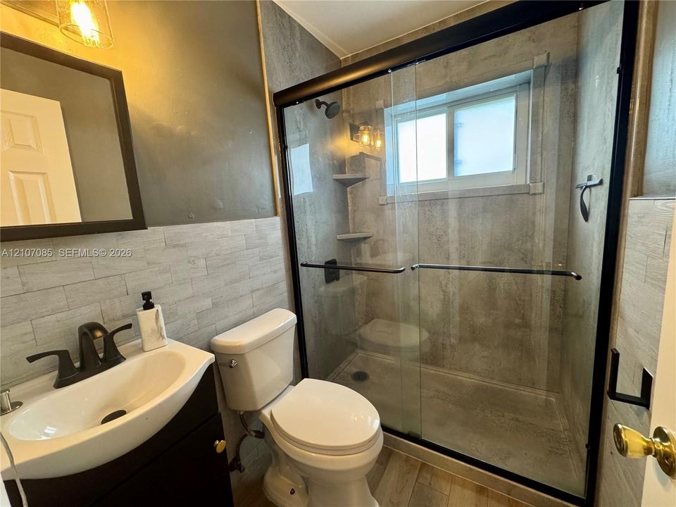 Bathroom featuring a walk-in shower with sliding glass doors, matte black fixtures, textured wall tile, and a vessel sink with a dark-finish vanity