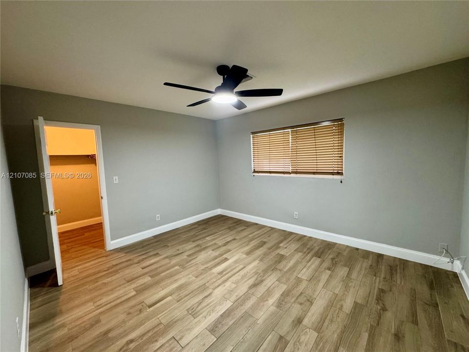 Neutral-toned interior room featuring wood-finish flooring, a ceiling fan with integrated lighting, and horizontal window blinds