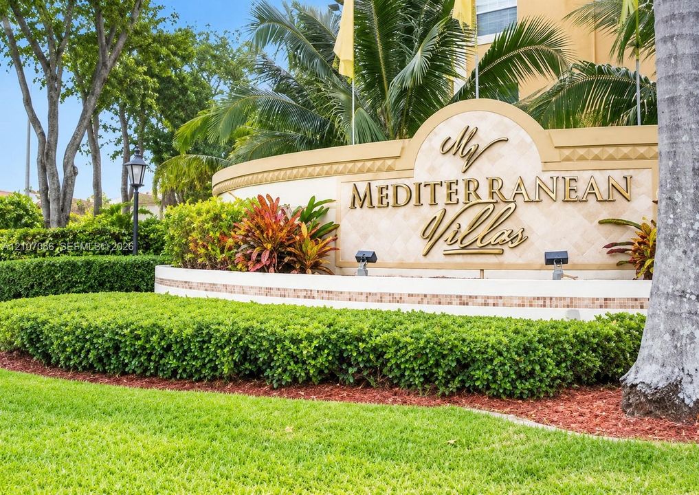 Community monument signage featuring dimensional gold-tone lettering, decorative stone masonry, integrated ground lighting, and professional perimeter landscaping with manicured shrubbery
