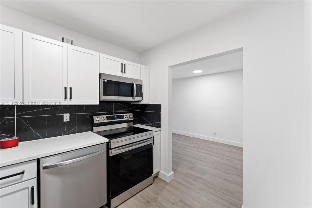 Kitchen featuring white shaker-style cabinetry, stainless steel appliances, dark stone-style backsplash, and white countertops