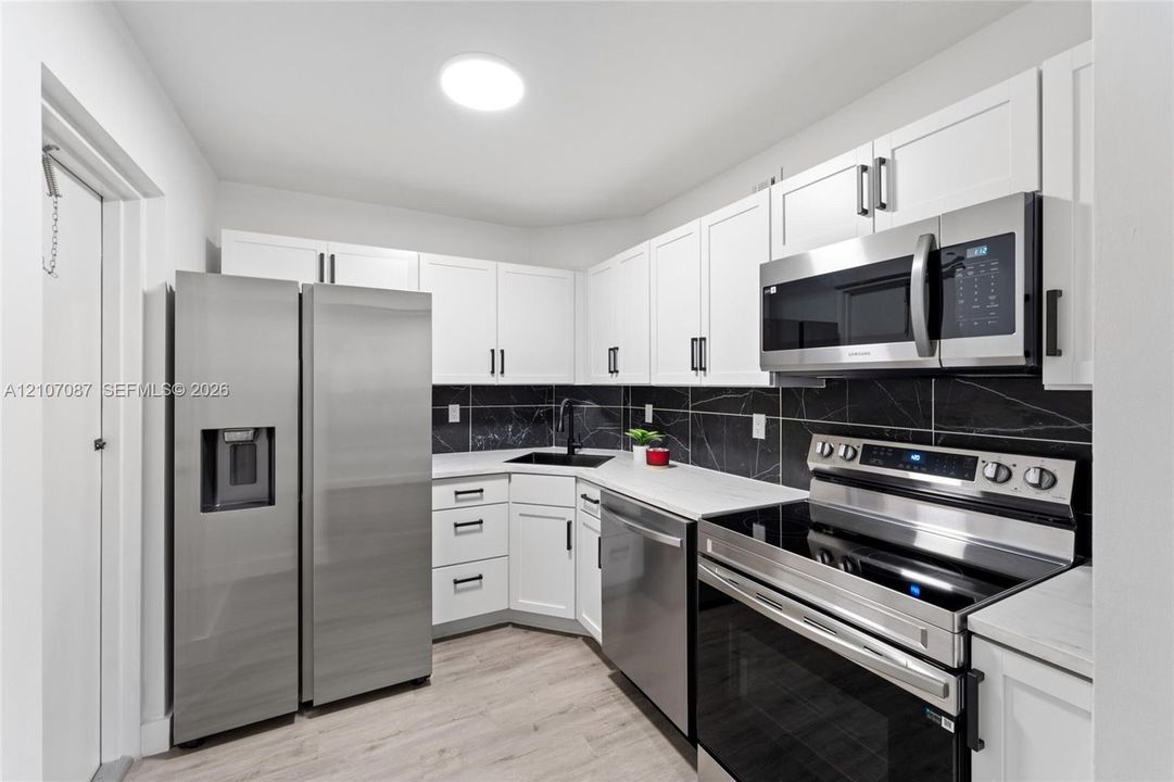 Kitchen featuring white cabinetry, stainless steel appliances, black tile backsplash, light-toned wood-finish flooring, and a dark-finish faucet