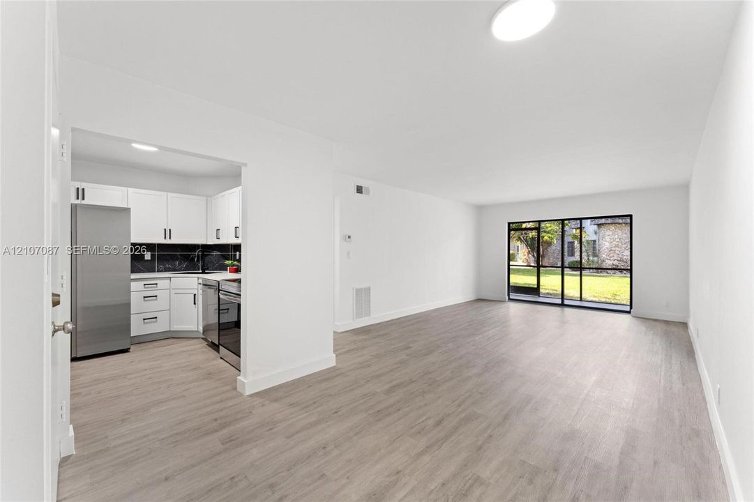 Kitchen featuring white shaker cabinetry, stainless steel appliances, and dark tile backsplash, complemented by wood-finish flooring and floor-to-ceiling glass sliding doors