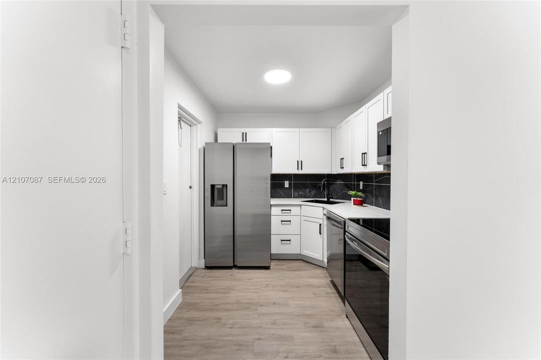 Kitchen featuring white shaker-style cabinetry, stainless steel appliances, dark stone-finish backsplash, matte black hardware, and wood-finish flooring
