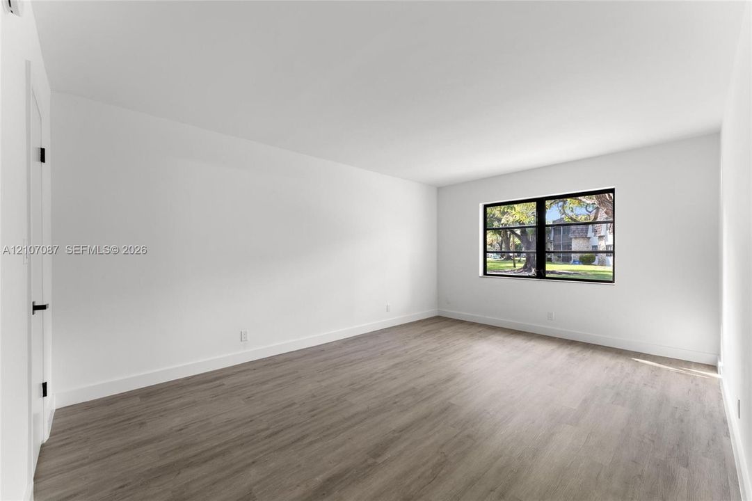 Neutral-toned wood-finish flooring, crisp white walls, and a large window featuring a black frame