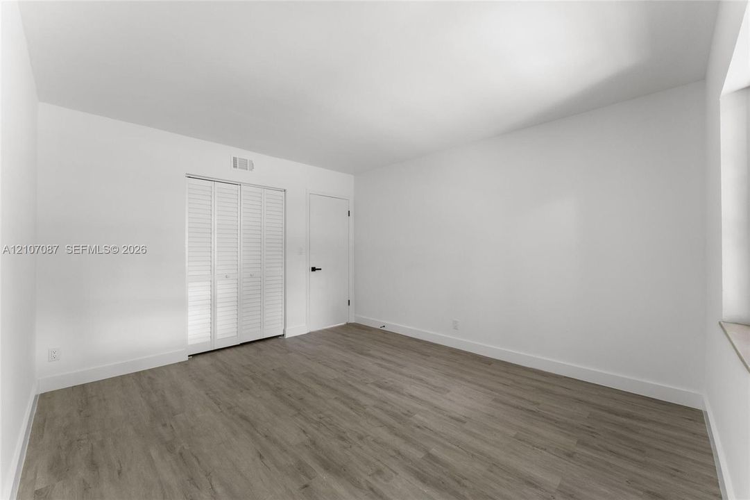 Room featuring wood-finish flooring, white walls, and a closet with white louvered bifold doors