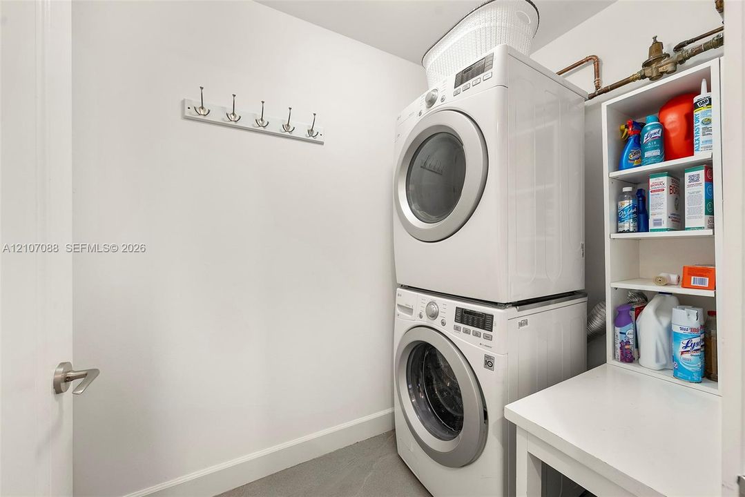 Laundry area featuring a stacked washer and dryer, built-in open shelving, and a wall-mounted hook rack