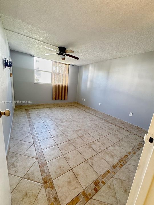 Interior room featuring neutral-toned walls, tile flooring with a decorative tile border, a window, and a ceiling fan