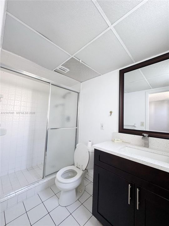 Bathroom featuring a dark-finish vanity with a stone-composite countertop, integrated sink, framed wall mirror, shower with a glass sliding enclosure, and tiled flooring