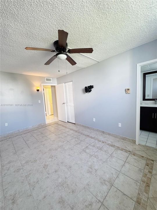 Ceramic tile flooring with decorative inlay border, textured ceiling, central ceiling fan, and louvered closet door