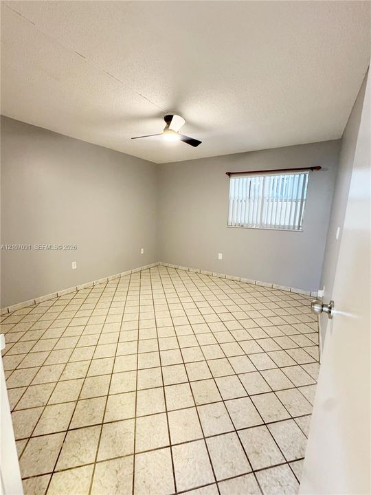 Neutral-toned room featuring tiled flooring, a ceiling fan with integrated lighting, and a window with vertical blinds