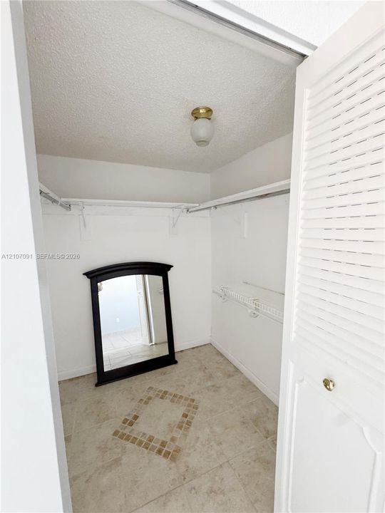 Walk-in closet featuring white wire shelving, neutral stone-finish tile flooring with a decorative inlay pattern, louvered bi-fold doors, and a flush-mount globe light fixture