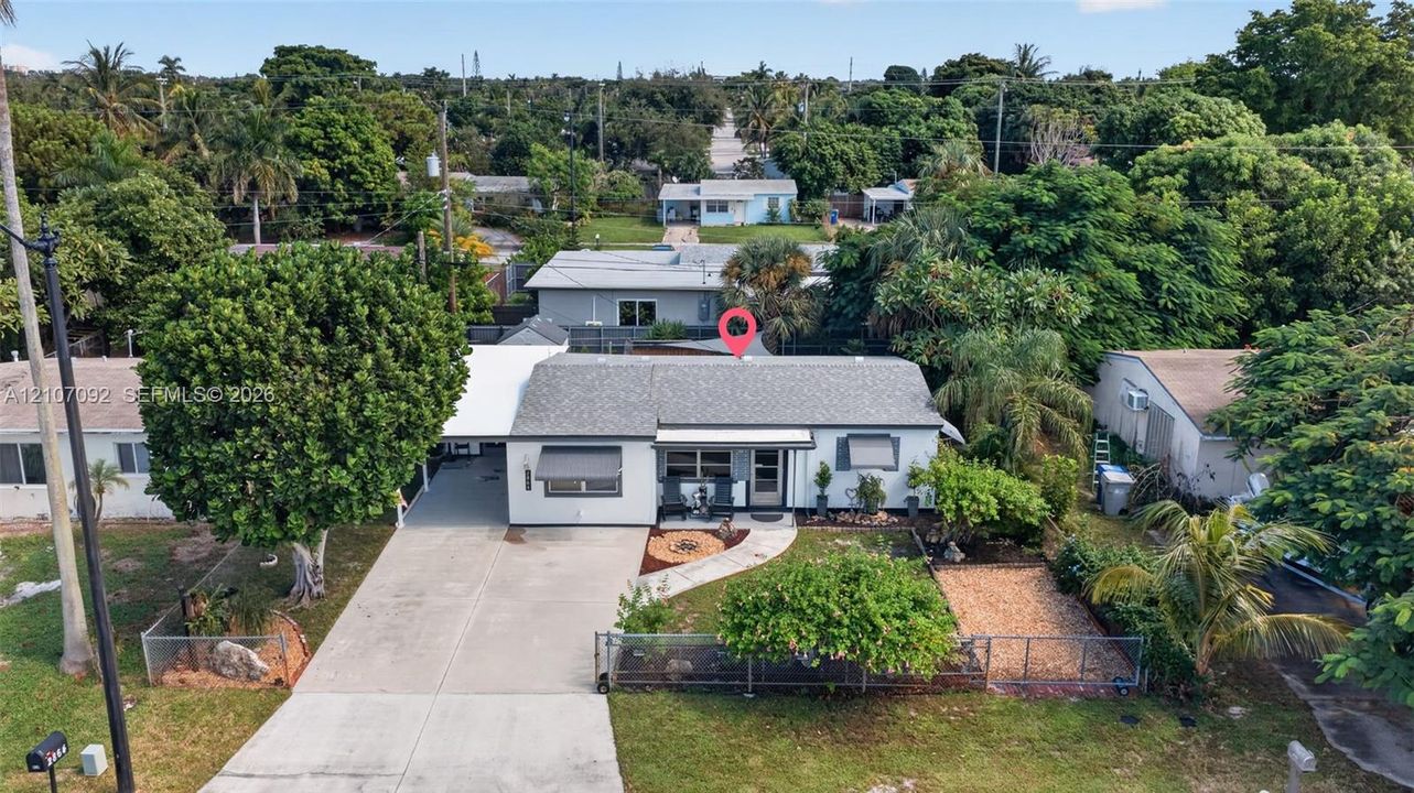Single-story residence featuring a concrete driveway, attached carport, metal awnings, fenced front yard, and mature landscaping