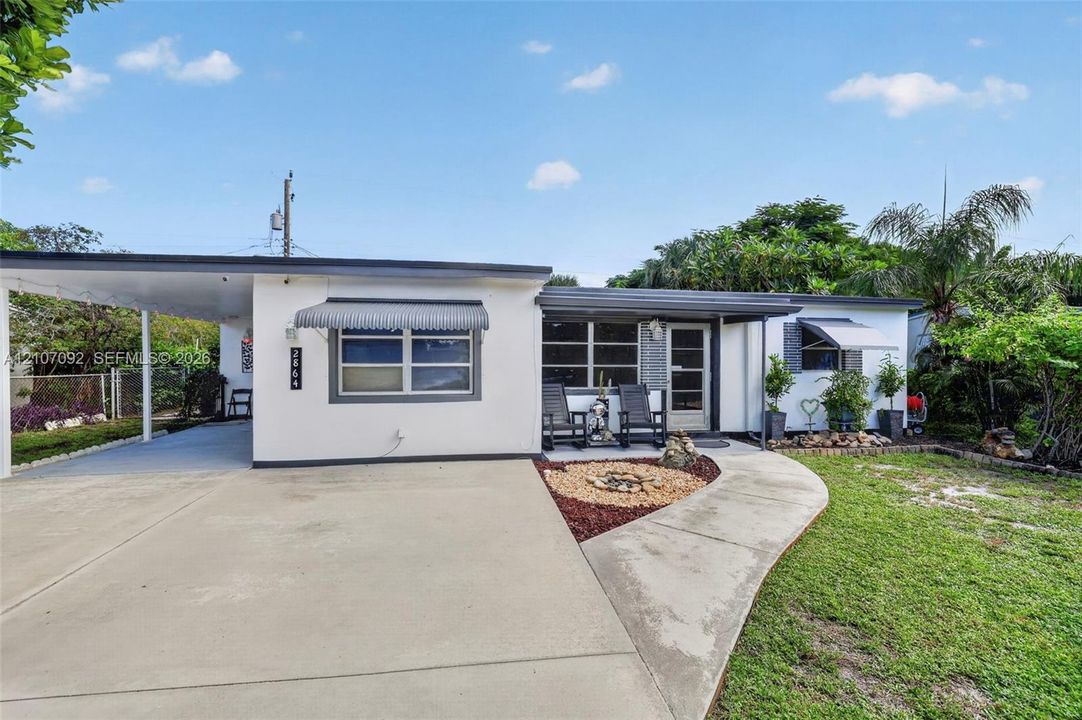 Exterior featuring a covered carport, concrete driveway, metal window awnings, and a landscaped front yard with decorative stone mulch