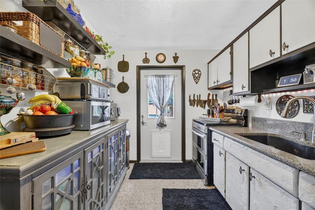 Kitchen featuring two-tone cabinetry with glass-panel doors, dark stone-finish countertops, an undermount sink with a gooseneck faucet, open shelving, and a glass-paneled exterior door