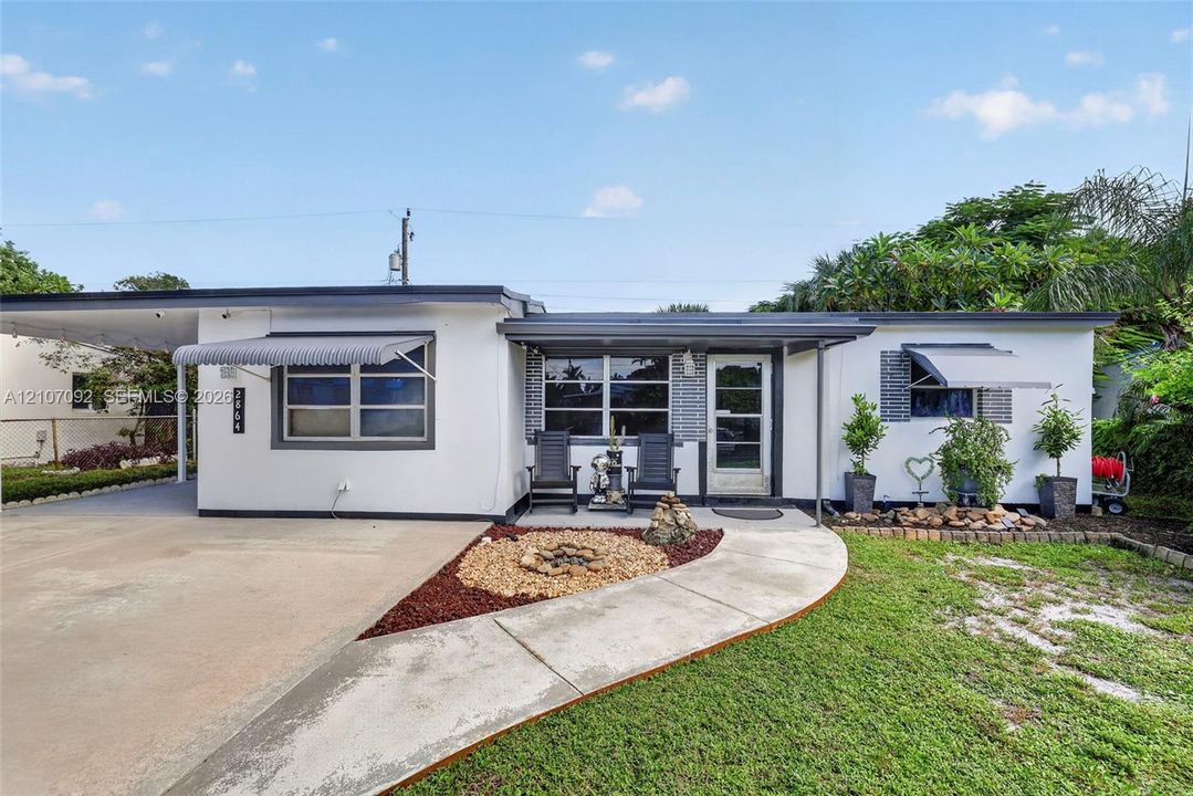 Mid-century modern exterior featuring a smooth stucco facade, metal-frame windows with retractable awnings, an attached carport, and a concrete walkway