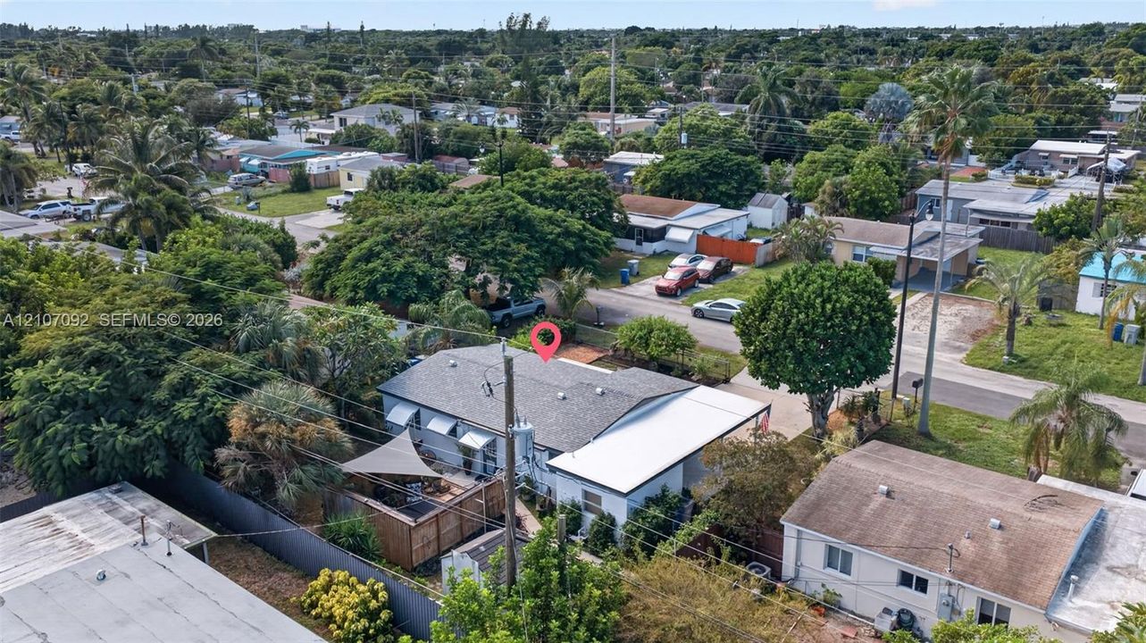 Aerial perspective of a single-story residence featuring a shingled roof, an attached carport, and a fenced rear yard with mature trees and foliage